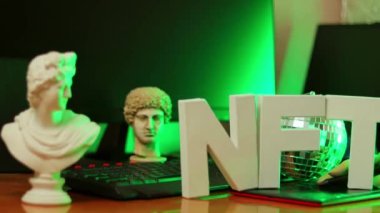 Tasarımcının işyerinde NFT yazıları ve yapay el. Parası ödenmeyen, neon ışıklı harfler. Gelecekçi kripto para birimi konsepti. Dönen kamera görüntüsü