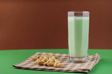 Healthy pistachio milk on a green-brown background. Vegan milk made from pistachios in a tall glass on a linen napkin. Copy space