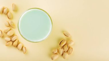 Pistachio milk in a glass and dried pistachios on a pastel yellow background. Pistachio lactose free milk for dietary nutrition. Top view