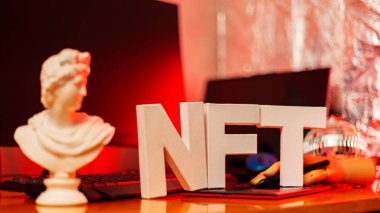 NFT inscription and artificial hand at the designer's workplace. Non-Fungible token lettering in neon light. Futuristic cryptocurrency concept