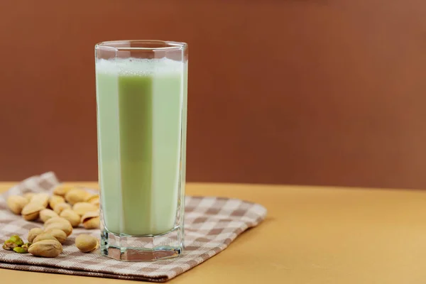 Plant-based natural pistachio milk on a beige background. Tall glass with pistachio milk on a linen napkin. Copy space