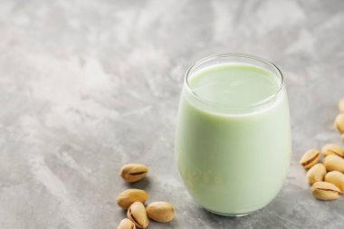 Organic non dairy pistachio milk in glass with pistachionuts on gray background. Vegan plant based milk. Copy space