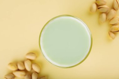 Pistachio milk in a glass and dried pistachios on a pastel yellow background. Pistachio lactose free milk for dietary nutrition. Top view