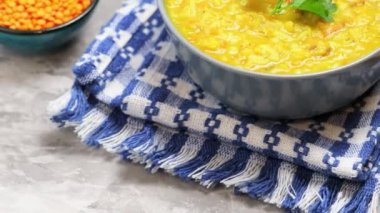 Kırmızı mercimek çorbası ve gri arka planda malzemeler. Bir kase mercimek çorbası ve keten peçetenin üzerinde tahta bir kaşık. Kamera hareketini yukarı kaldır