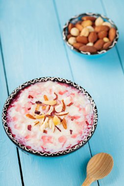 Fındıklı ve gül sulu lezzetli sütlaç. Bir kase Hint kheer sütlacı boyalı mavi tahtalarda. Ramazan Kareem ve iftar müslüman yemekleri