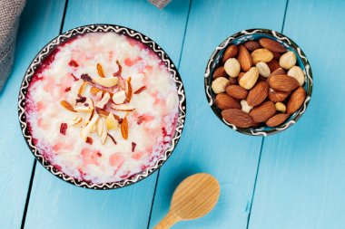 Fındıklı ve gül sulu lezzetli sütlaç. Bir kase Hint kheer sütlacı boyalı mavi tahtalarda. Ramazan Kareem ve iftar müslüman yemekleri