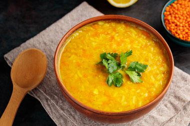 Koyu arkaplanda kırmızı mercimek Hint çorbası. Bir kase mercimek çorbası, malzemeler ve tahta kaşık. Kapat.