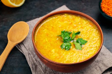 Koyu arkaplanda kırmızı mercimek Hint çorbası. Bir kase mercimek çorbası, malzemeler ve tahta kaşık. Kapat.