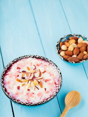 Fındıklı ve gül sulu lezzetli sütlaç. Bir kase Hint kheer sütlacı boyalı mavi tahtalarda. Ramazan Kareem ve iftar müslüman yemekleri