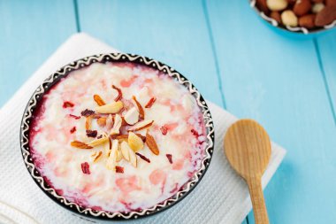 Fındıklı ve gül sulu lezzetli sütlaç. Bir kase Hint kheer sütlacı boyalı mavi tahtalarda. Ramazan Kareem ve iftar müslüman yemekleri