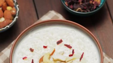 Tahta bir tahtanın üzerinde pirinç kheer, fındık ve kurutulmuş amber çiçeği. Fındıklı Hint kheer sütlacı. Havan topu müslüman yemeği konsepti. Kamera hareketini aşağı eğ