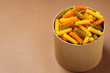 Karton bir kutuda üç renkli fusilli makarna. Bej arka planda çiğ fusilli makarna. Boşluğu kopyala