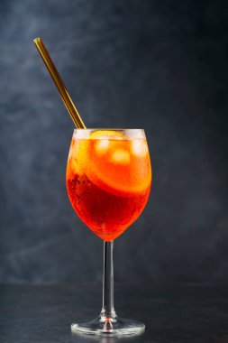 Karanlık arka planda Aperol Spritz kokteyli. Kokteyl Aperol Spritz, portakallı ve buzlu, çevre dostu cam pipetli.