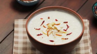 Tahta arka planda sütlaçlı kase. Kheer 'in fındık ve amberle süslenmiş kremalı pirinci. Popüler Ramazan yemeği. Dönen kamera görüntüsü