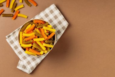 Keten peçetede üç renkli fusilli makarna. Çevre kutusunda yeşil, turuncu ve sarı fusilli makarna depolanmış. Boşluğu kopyala