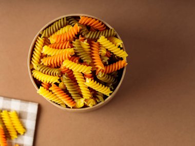 Keten peçetede üç renkli fusilli makarna. Çevre kutusunda yeşil, turuncu ve sarı fusilli makarna depolanmış. Boşluğu kopyala
