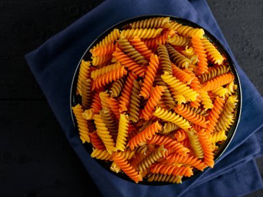 Mavi keten peçeteye üç renk rotini veya fusilli makarna. Tahta bir tabakta renkli İtalyan çiğ makarnası. Kapat.