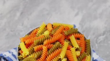 Gri arka planda çiğ İtalyan fusilli makarna. Kasede üç renkli fusilli makarna. Kamera hareketini aşağı eğ