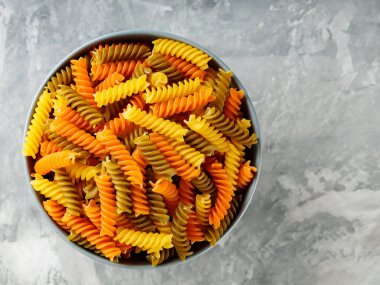 Gri arka planda ıspanaklı ve domatesli Fusilli makarna. Bir kasede çiğ İtalyan fusili makarna. Üst Manzara. Boşluğu kopyala