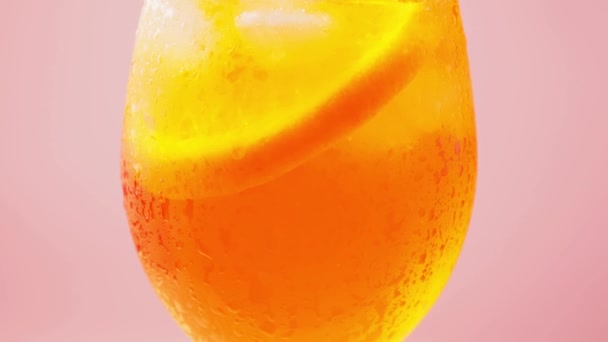 ピンクの背景にアペロール スプリッツのカクテルのグラス オレンジと氷をガラスにしたアペロスピッツカクテル 閉じろ — ストック動画