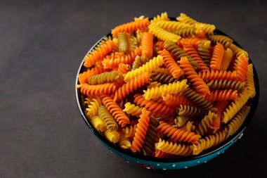 Fusilli kuru makarna koyu arkaplanda. Kasede üç renkli fusilli makarna. Üst Manzara. Boşluğu kopyala