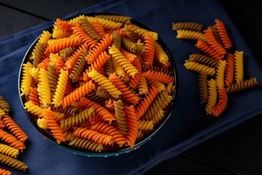 Mavi keten peçeteye üç renk rotini veya fusilli makarna. Tahta bir tabakta renkli İtalyan çiğ makarnası. Kapat.