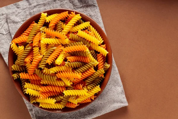 Renkli fusilli makarna ve bej arka planda buğday. Kil kasede çok renkli spiral makarna. Boşluğu kopyala