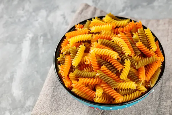 Fusilli kuru makarna ve beton kasesi. Keten peçetede renkli İtalyan çiğ makarnası. Boşluğu kopyala