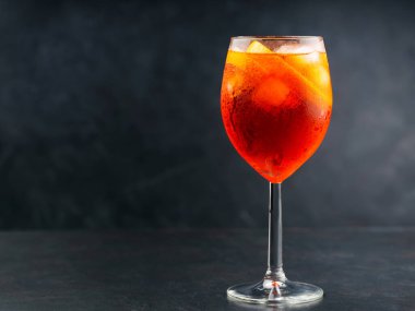 Bardakta Aperol Spritz kokteyli ve koyu arkaplanda taze turuncu. Şarap kadehinde servis edilen bir bardak buz gibi Aperol Spritz kokteyli. Boşluğu kopyala