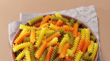 Bej arka planda çiğ İtalyan fusilli makarna. Kil tabakta üç renkli fusilli makarna. Kamera hareketini aşağı eğ