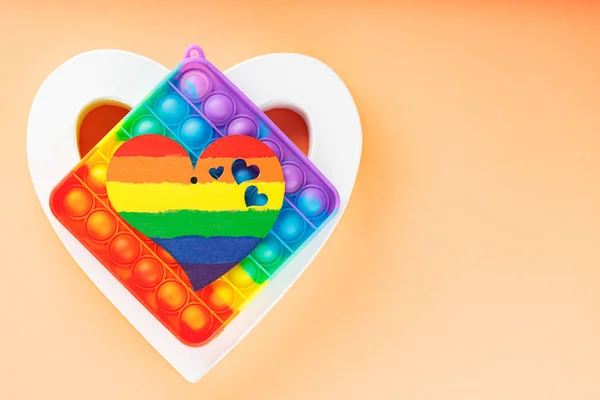 Rainbow heart, white heart and pop it toy on coral background. LGBT equal rights movement and gender equality concept. Copy space