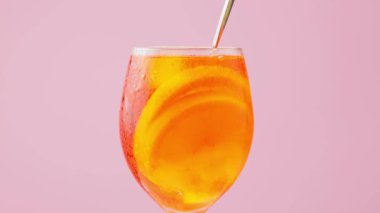 Aperol Spritz 'i kokteyl kaşığıyla karıştırmak. Pembe arka planda bir bardak Aperol Spritz kokteyli. Yaz ferahlatıcı içecek konsepti