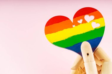 Gökkuşağı kalbi pembe arka planda cyborg elde. LGBT bayrağı renginde bir kalp tutan tahta el. LGBT Gurur Ayı konsepti. Boşluğu kopyala