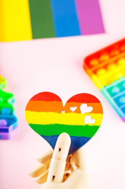 Pembe arka planda LGBT bayrağı renginde kalp. Yapay kol gökkuşağı kalbini tutar. LGBT Gurur ayı konsepti