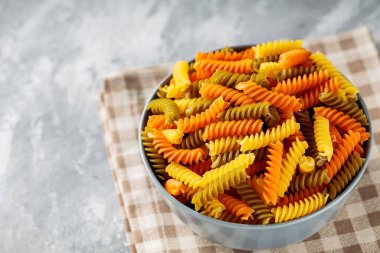 Beton üzerine çiğ fusilli makarna. Keten peçeteye üç renk rotini veya fusilli makarna. İtalyan yemeği.