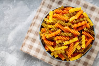 Beton üzerine çiğ fusilli makarna. Keten peçeteye üç renk rotini veya fusilli makarna. İtalyan yemeği.