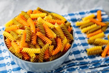 Beton üzerine çiğ fusilli makarna. Keten peçetede renkli İtalyan çiğ makarnası. İtalyan mutfağı