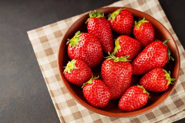 Keten peçetenin üzerinde olgun bir çilek kasesi. Koyu arkaplanda taze toplanmış çilekler. Boşluğu kopyala