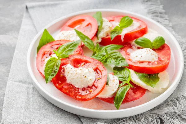 Gri keten peçeteli beyaz tabakta servis edilen gurme Caprese Salatası. Kapat.