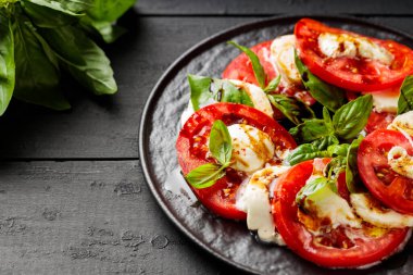Olgun domatesli lezzetli caprese salatası, mozzarella peyniri ve koyu ahşap tahtalarda taze fesleğen yaprağı. Kapat.