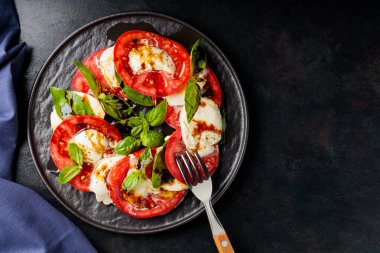 Dilimlenmiş domatesli İtalyan caprese salatası, mozzarella, fesleğen, koyu arkaplanda zeytinyağı. Uzayı kopyala Üst görünüm