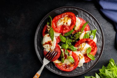 Dilimlenmiş domatesli İtalyan caprese salatası, mozzarella, fesleğen, koyu arkaplanda zeytinyağı. Uzayı kopyala Üst görünüm