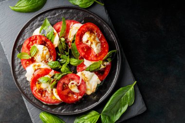 İtalyan caprese salatası, mozzarella, domates ve fesleğen. Siyah tabakta sağlıklı klasik lezzetli Caprese salatası.