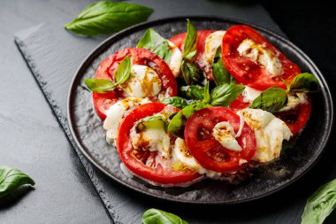 İtalyan caprese salatası, mozzarella, domates ve fesleğen. Siyah tabakta sağlıklı klasik lezzetli Caprese salatası.