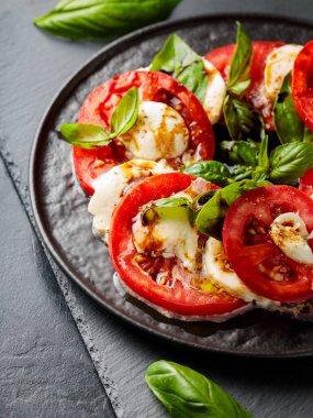 İtalyan caprese salatası, mozzarella, domates ve fesleğen. Siyah tabakta sağlıklı klasik lezzetli Caprese salatası.