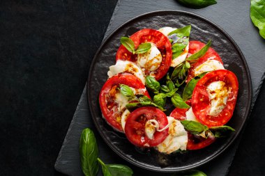 İtalyan caprese salatası, mozzarella, domates ve fesleğen. Siyah tabakta sağlıklı klasik lezzetli Caprese salatası.