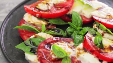 Domatesli İtalyan Caprese Salatası, mozzarella ve siyah tabakta fesleğen. Dönen kamera görüntüsü