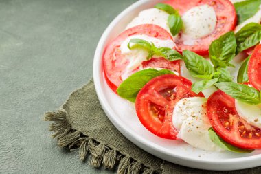 Domatesli salata, mozzarella ve yeşil arka planda fesleğen. Kapat.