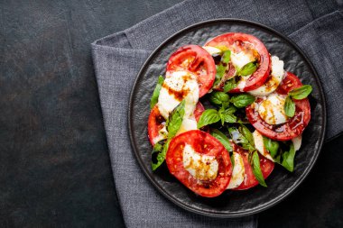 Dilimlenmiş taze domateslerden yapılmış Caprese salatası, siyah tabakta servis edilen mozzarella peyniri ve fesleğen. Üst Manzara. Boşluğu kopyala