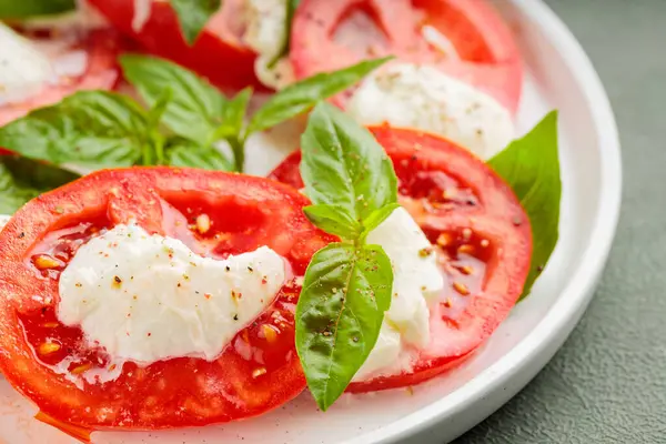 Domatesli salata, mozzarella ve yeşil arka planda fesleğen. Kapat.